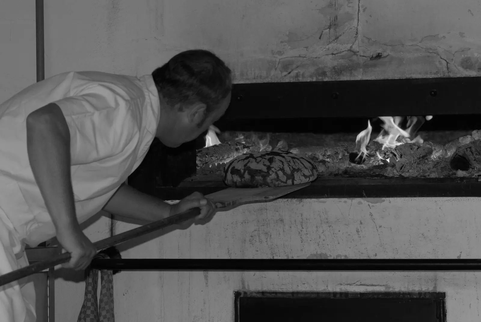 Bäcker setzt ein Brot mit dem Schieber in den Holzofen ein
